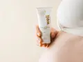 En hand håller en tub med "well Nipple & Barrier Cream", liknande Medela Purelan, nära en gravid mage.
