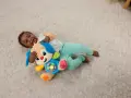 Ett litet barn skrattar och kramar sin Fisher Price hund på en ljus matta. Hunden har blå öron och en färgglad mage med knappar.