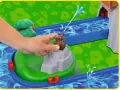 En hand aktiverar en vattenpump på en Aquaplay mountain lake-lekplats, som sprutar vatten genom en blå kanal.