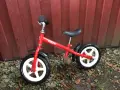 En röd stiga springcykel står lutad mot en röd trävägg. Den har vita fälgar och svarta däck.