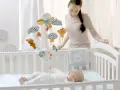 En mamma tittar på sin bebis i en spjälsäng med en mobil som har djurfigurer. En tiny love into the forest-dröm för den lilla.