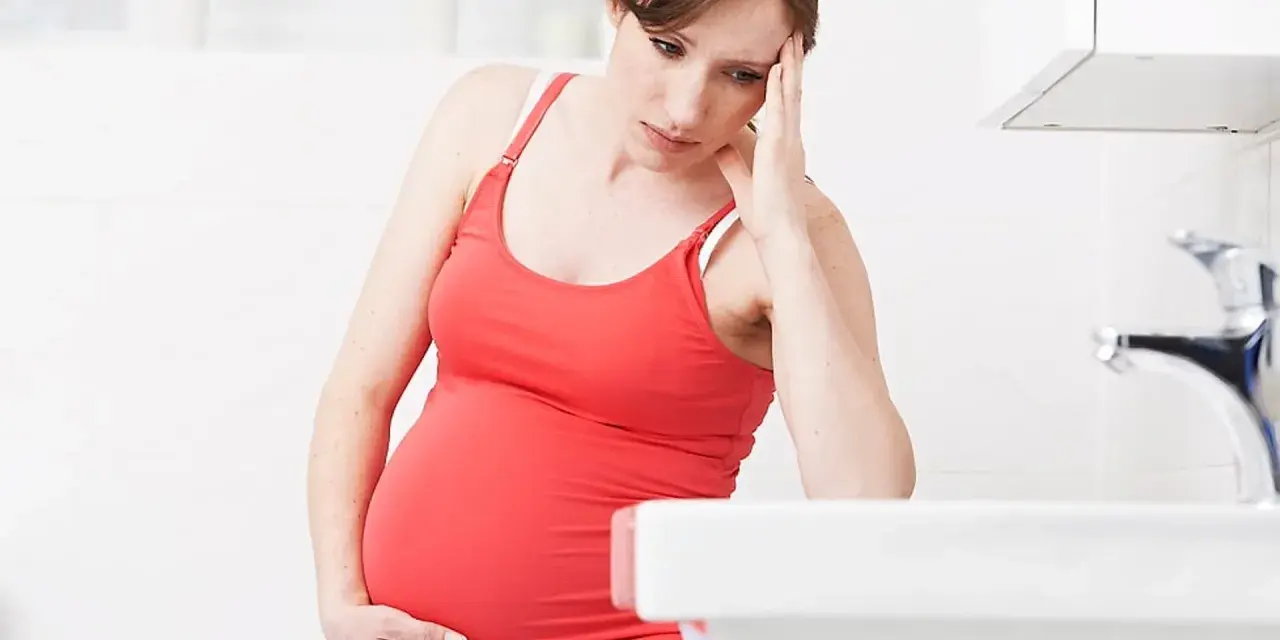 Gravid kvinna med handen mot pannan, känner sig illamående sent i graviditeten.