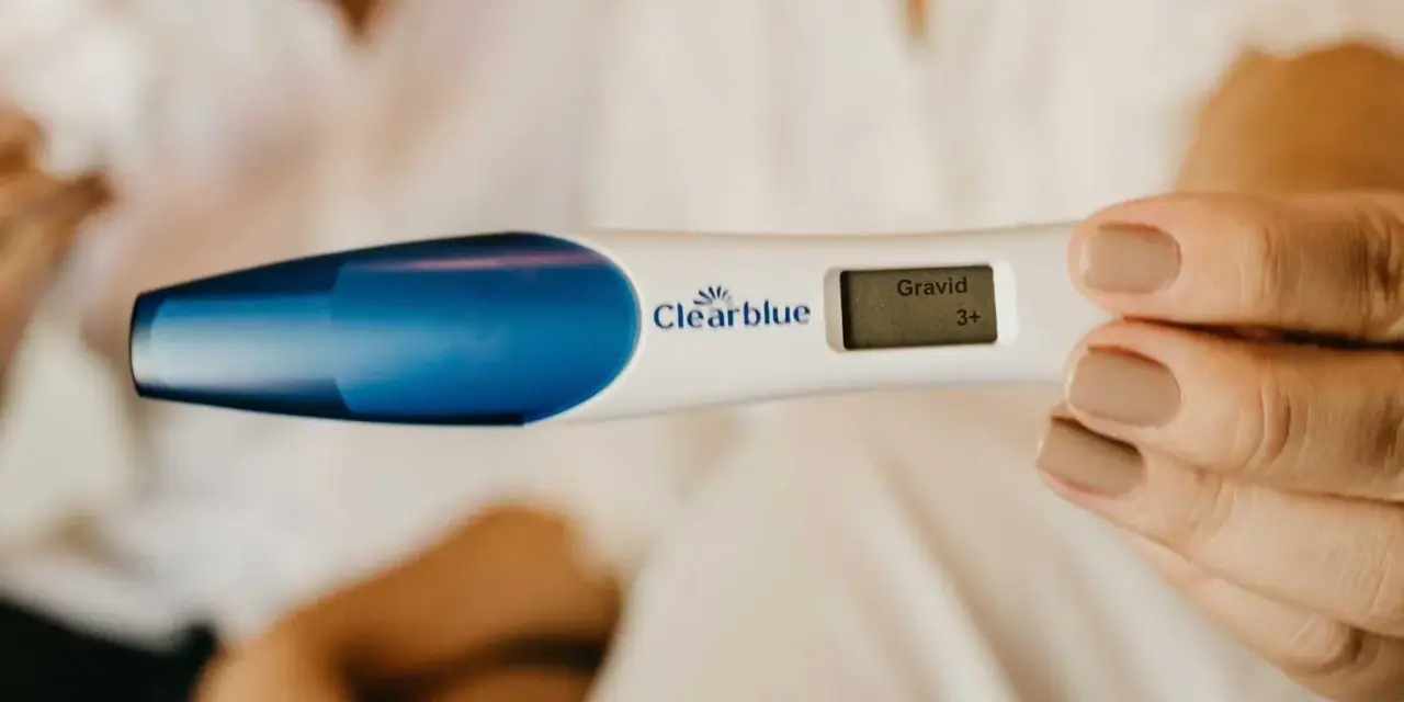 En hand håller en graviditetstest som visar "Gravid 3+". Tidiga tecken på graviditet kan vara spännande.