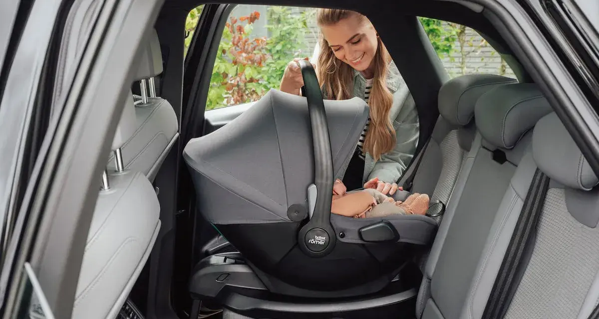 En leende mamma placerar en baby i en Britax Baby Safe Core bilbarnstol i en bil.