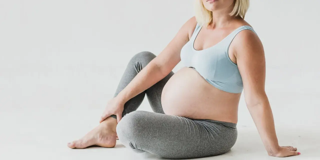 Gravid kvinna med stor mage sitter på golvet, håller om sitt ben. Kanske upplever hon myrkrypningar i benen gravid.
