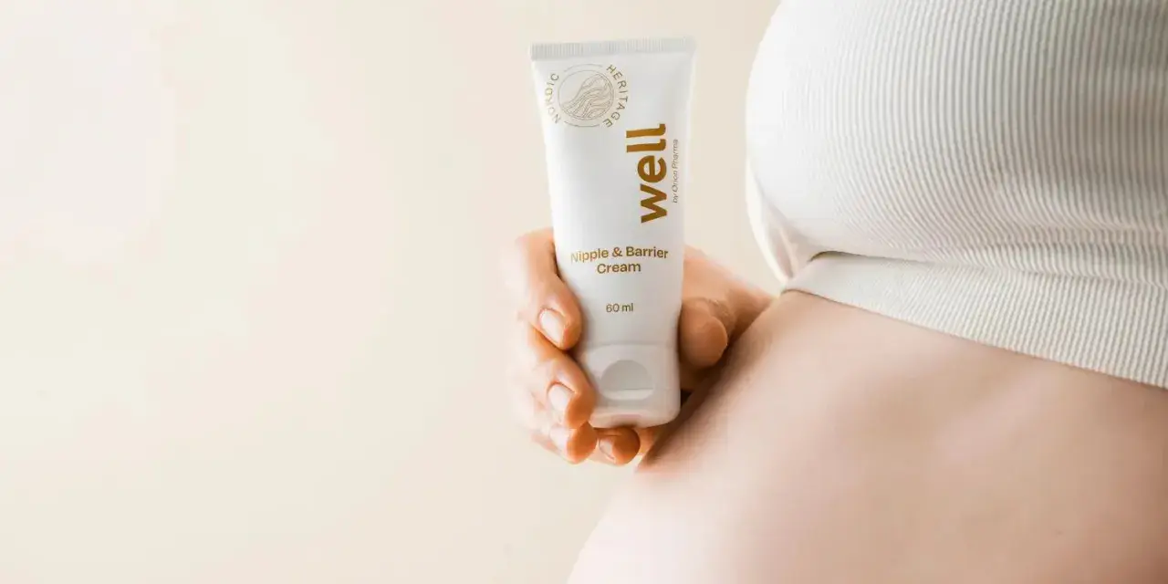 En hand håller en tub med "well Nipple & Barrier Cream", liknande Medela Purelan, nära en gravid mage.