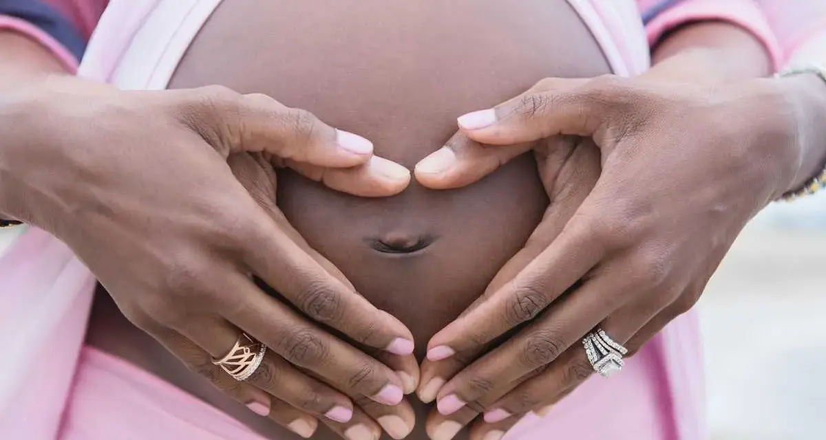 Gravid vecka 32, familjeliv. Händer formar ett hjärta runt magen.