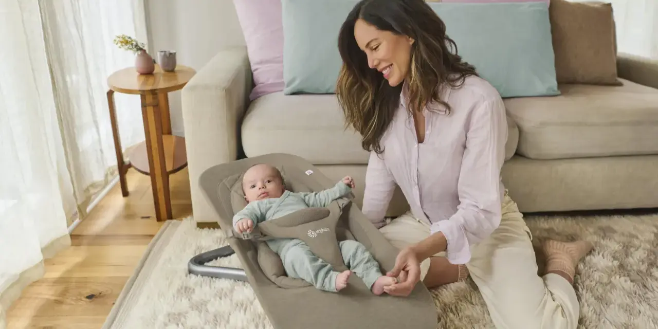 En leende mamma interagerar med sin bebis i en ergobaby babysitter.