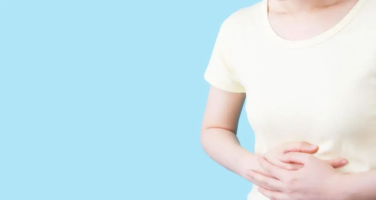 Kvinna håller sig om magen, upplever obehag som kan liknas vid IBS, graviditet eller magproblem.