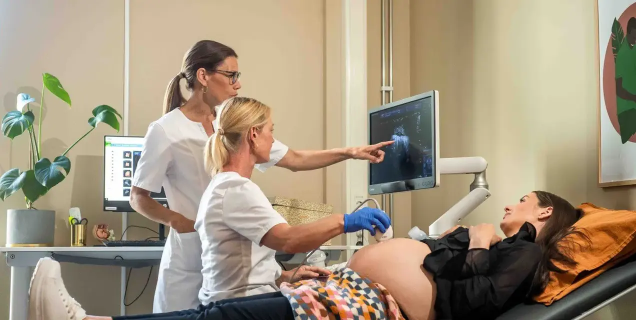 Två vårdgivare utför ett vaginalt ultraljud på en gravid kvinna. Bilden visar en skärm med ultraljudsbilder.