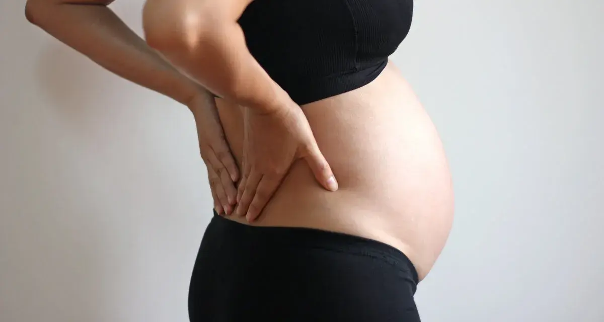 Gravid kvinna med händerna på ryggen, upplever ont i revbenen tidigt i graviditeten.