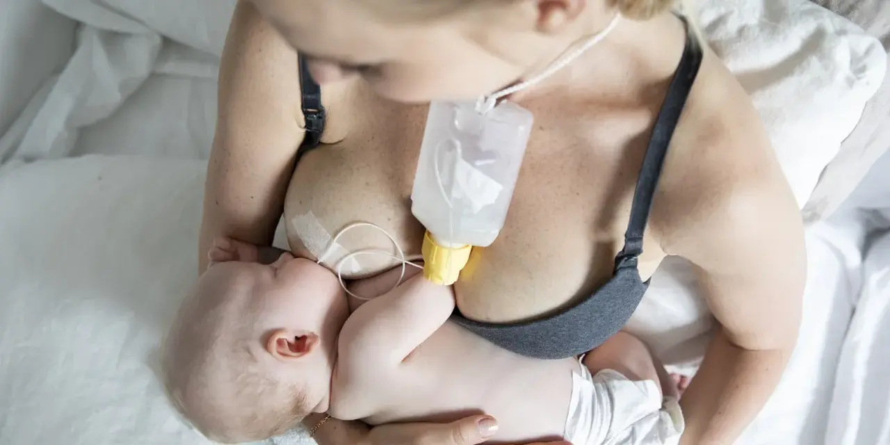 En mamma matar sitt barn med en flaska som är fäst vid bröstet, med hjälp av ett bröstvårtsskydd för att underlätta amningen.