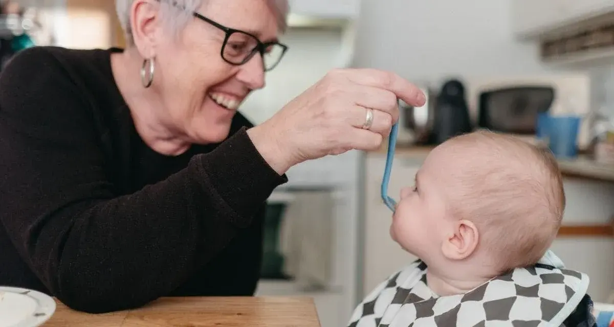 Glad mormor matar bebis med smakportioner. Första maten för en 4 månader gammal bebis.
