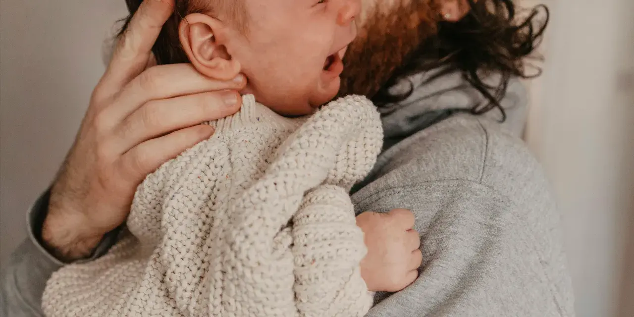 En bebis drar sig i håret medan den vilar i sin pappas famn.