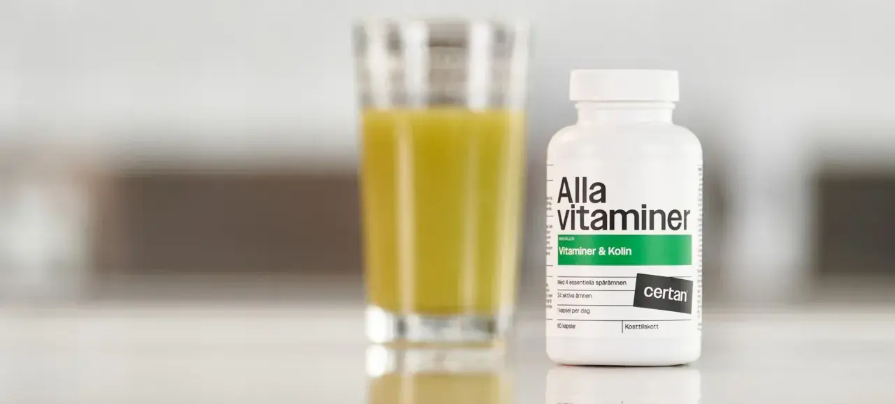 En flaska "Alla vitaminer" med texten "Vitaminer & Kolin" står bredvid ett glas med gul vätska. Perfekt för den som behöver extra vitaminer under graviditeten.