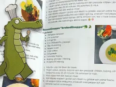 En glad krokodilkock med en sked i handen presenterar receptet på "Krokodilsoppa". En perfekt rese potta för små äventyrare!