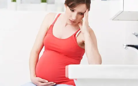 Gravid kvinna med handen mot pannan, känner sig illamående sent i graviditeten.