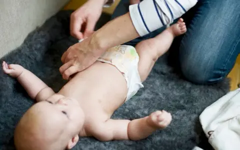 En person byter blöja på en bebis. Frågan "hur ofta bajsar bebis" är relevant för många föräldrar.