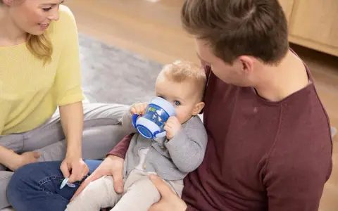 En bebis dricker ur en blå nuk magic cup medan föräldrarna tittar på.