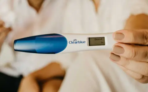 En hand håller en graviditetstest som visar "Gravid 3+". Tidiga tecken på graviditet kan vara spännande.