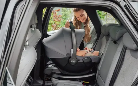 En leende mamma placerar en baby i en Britax Baby Safe Core bilbarnstol i en bil.