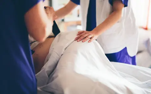 Två vårdgivare assisterar en gravid v 39. En av dem håller i en apparat, den andra lägger en hand på magen.