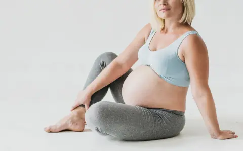 Gravid kvinna med stor mage sitter på golvet, håller om sitt ben. Kanske upplever hon myrkrypningar i benen gravid.