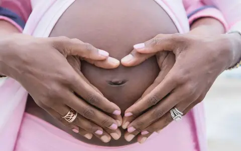 Gravid vecka 32, familjeliv. Händer formar ett hjärta runt magen.