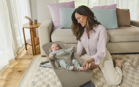 En leende mamma interagerar med sin bebis i en ergobaby babysitter.