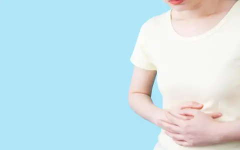 Kvinna håller sig om magen, upplever obehag som kan liknas vid IBS, graviditet eller magproblem.