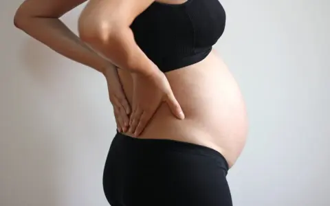 Gravid kvinna med händerna på ryggen, upplever ont i revbenen tidigt i graviditeten.