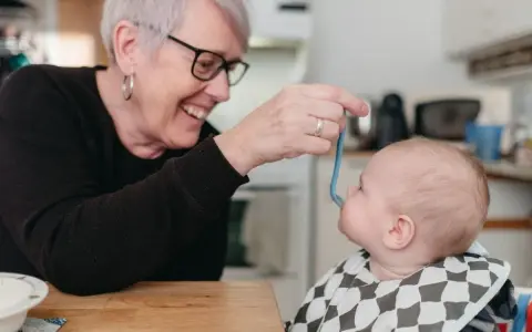 Glad mormor matar bebis med smakportioner. Första maten för en 4 månader gammal bebis.