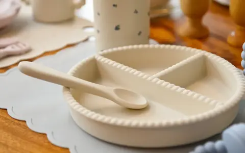 En ljusbeige tallrik med sugpropp och en sked ligger på ett ljusblått underlägg.