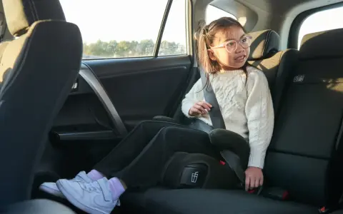 Flicka i bilens baksäte sitter på bälteskuddar och är fastspänd.