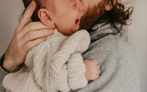 En bebis drar sig i håret medan den vilar i sin pappas famn.
