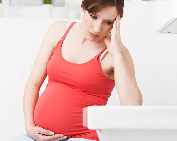 Gravid kvinna med handen mot pannan, känner sig illamående sent i graviditeten.