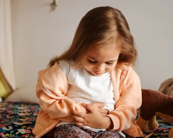 Liten flicka med magont, kanske bebis diarre. Hon sitter på en säng med händerna på magen.