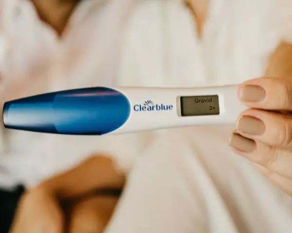 En hand håller en graviditetstest som visar "Gravid 3+". Tidiga tecken på graviditet kan vara spännande.