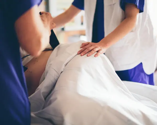 Två vårdgivare assisterar en gravid v 39. En av dem håller i en apparat, den andra lägger en hand på magen.