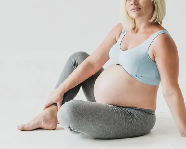 Gravid kvinna med stor mage sitter på golvet, håller om sitt ben. Kanske upplever hon myrkrypningar i benen gravid.