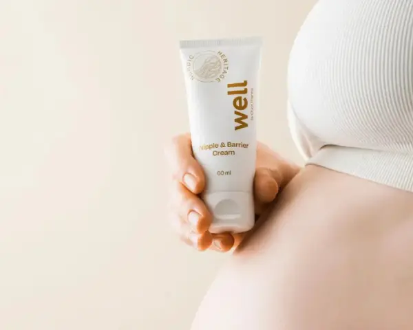 En hand håller en tub med "well Nipple & Barrier Cream", liknande Medela Purelan, nära en gravid mage.