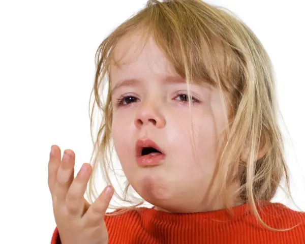 Ett litet barn med rött linne och blont hår, med tårfyllda ögon och öppen mun, som om det hostar på natten.