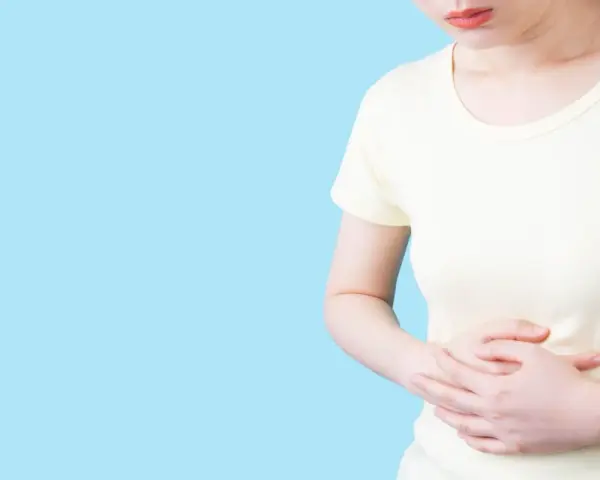 Kvinna håller sig om magen, upplever obehag som kan liknas vid IBS, graviditet eller magproblem.