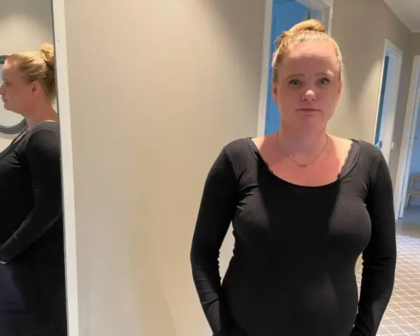 Gravid kvinna med stressad blick, med sin mage synlig. Hon funderar på hur hon ska hantera gravid stress på jobb.