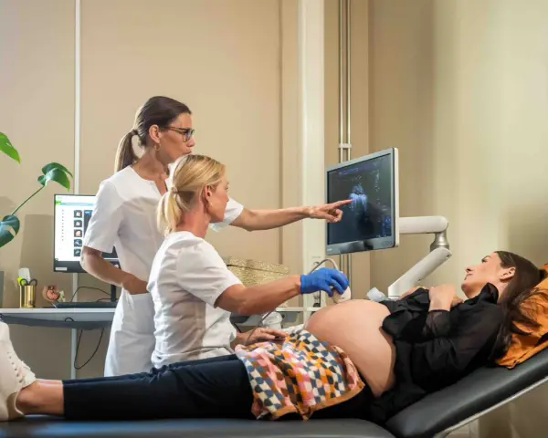 Två vårdgivare utför ett vaginalt ultraljud på en gravid kvinna. Bilden visar en skärm med ultraljudsbilder.