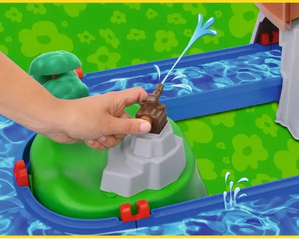 En hand aktiverar en vattenpump på en Aquaplay mountain lake-lekplats, som sprutar vatten genom en blå kanal.
