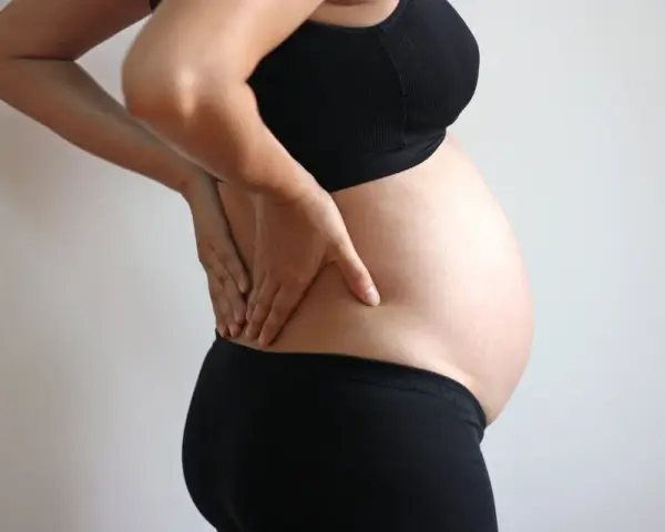 Gravid kvinna med händerna på ryggen, upplever ont i revbenen tidigt i graviditeten.