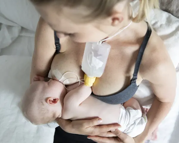 En mamma matar sitt barn med en flaska som är fäst vid bröstet, med hjälp av ett bröstvårtsskydd för att underlätta amningen.