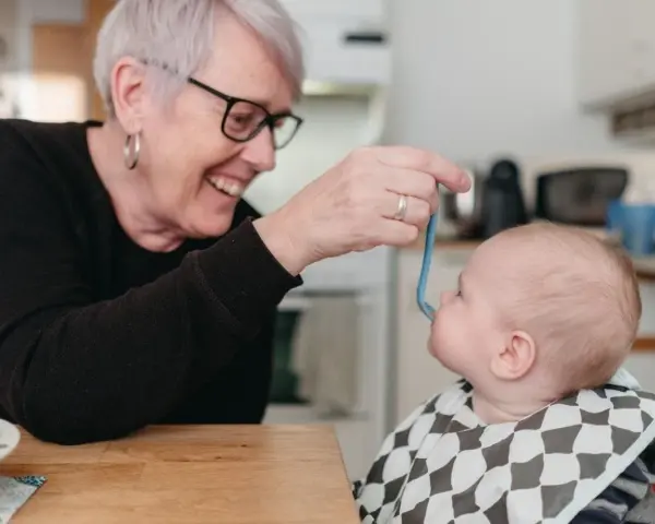Glad mormor matar bebis med smakportioner. Första maten för en 4 månader gammal bebis.