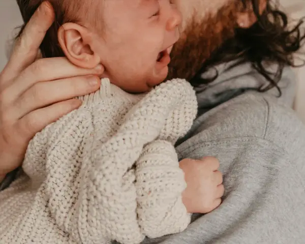 En bebis drar sig i håret medan den vilar i sin pappas famn.